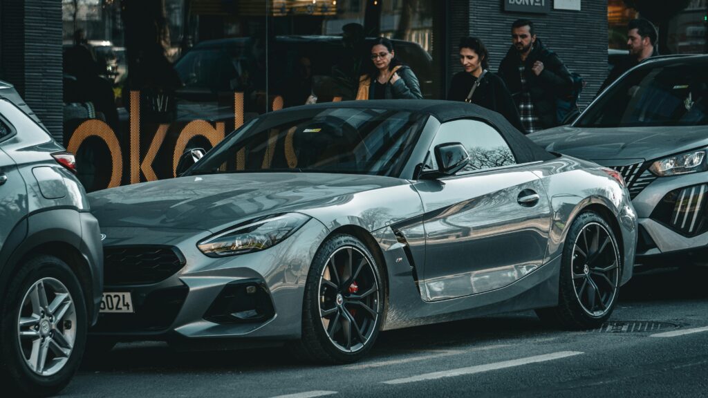 Gray BMW Z4 roadster parked on a bustling city street with people passing by, capturing urban lifestyle.