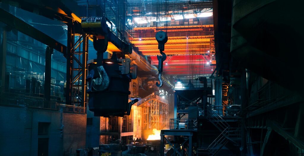 Inside a bustling steel factory with cranes and molten metal casting an intense glow.